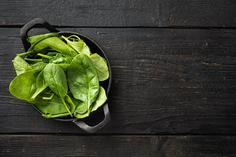 Bundle of fresh spinach, in frying cast iron pan or pot, on black wooden tabl Stock Photos