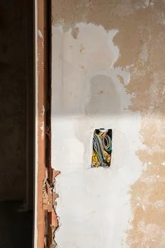A bundle of multi-colored tangled wires in a hole in a peeling wall in house Stock Photos