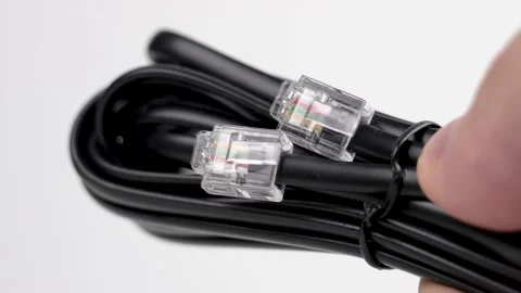 Bundle of a new black telephone cable with plugs in a hand on a white  스톡 동영상 204727522