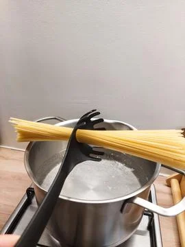 Bundle of raw spaghetti held diagonally by a black pasta spoon being placed into Stock Photos