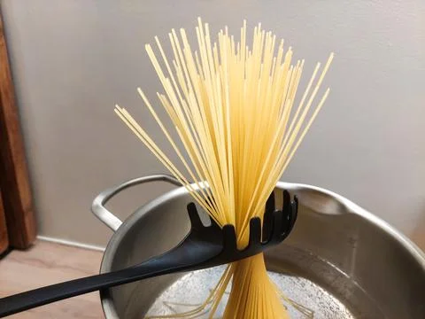 Bundle of raw spaghetti held diagonally by a black pasta spoon 스톡 사진