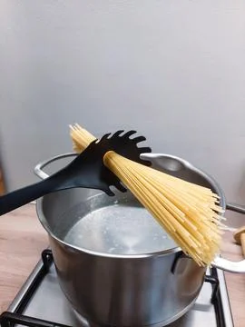Bundle of raw spaghetti held diagonally by a black pasta spoon being placed Stock Photos