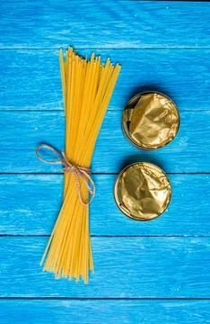 Bundle of spaghetti tied with string and two opened cans on wooden blue boards. Stock Photos