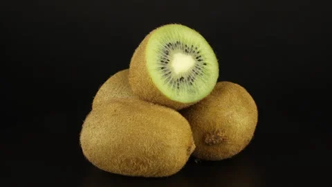 A bundle of two whole kiwi and two halves are rotating on a black background. Видео 151671517