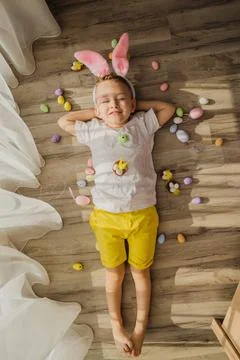 Bunny boy lying in room with easter eggs. Funny little Easter bunny child with Stock Photos