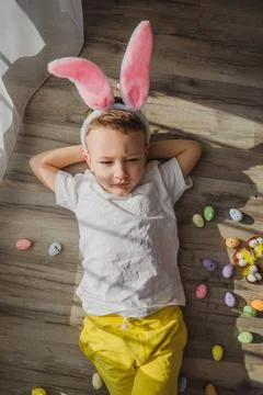 Bunny boy lying in room with easter eggs. Funny little Easter bunny child with Stock Photos