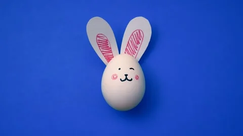 Bunny ears, cute rabbit face on white chicken egg on cornflower blue Stock Footage 331550662