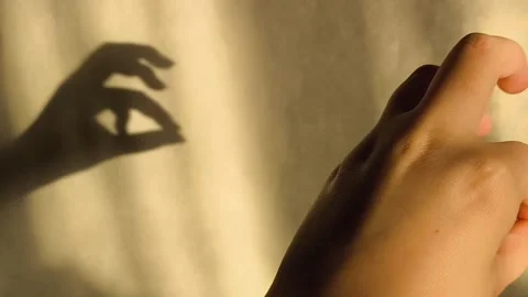 Bunny-shaped shadow on the wall from sunlight. The woman holds her fingers in Stock Footage 326122584