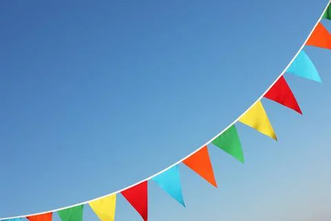 Bunting with colorful triangular flags against blue sky. Space for text Stock Photos