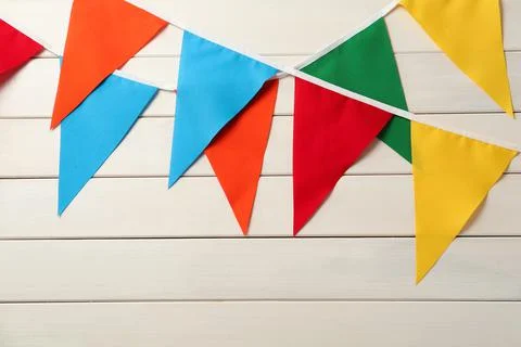 Buntings with colorful triangular flags hanging on white wooden wall. Festive Stock Photos