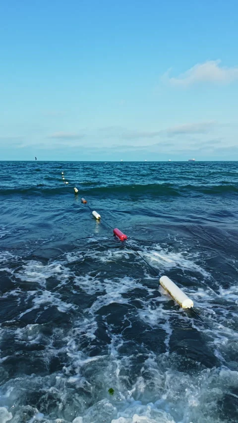 Buoys float on ocean waves near the shore under a blue sky with some clouds in Stock Footage 337911874