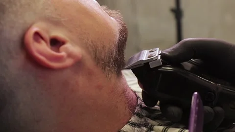 Burber cuts a client's beard using a shaving machine in a barbershop Video stock 142493080
