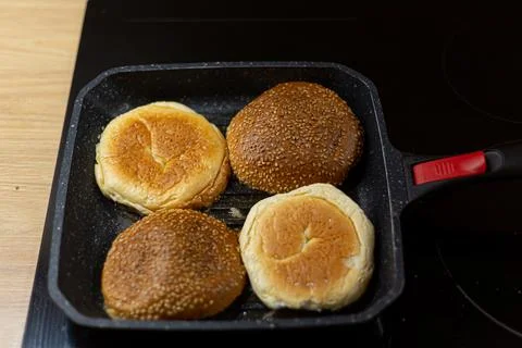 Burger bread with sesame is heating on a grill pan. Process of cooking self m Photos