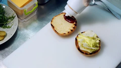 Burger cooking. Cook pours red sauce on a burger bun. 스톡 동영상 158334053
