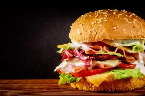 Burger with lettuce, cheese, ham and tomato on dark background. Stock Photos