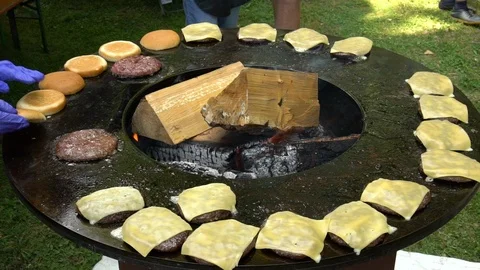 Burger meat, cheese and bread bake on outdoor grill with firewood. Handheld shot Stock Footage 109504495