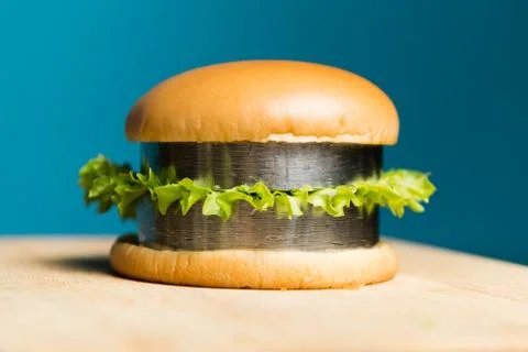 A burger with metal bars instead of cutlets lies on a wooden board. Eating ir Stock Photos