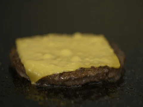 Burger patty with cheese slice being fried on commercial griddle in kitchen 動画素材 73548622