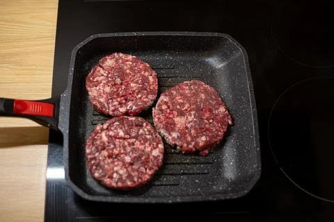 Burger raw minced beef meat cutlet on a grill pan. Process of cooking self ma Stock Photos