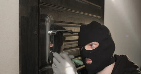 Burglar in balaclava inserts thin metal latchkey into keyhole Video stock 314717859