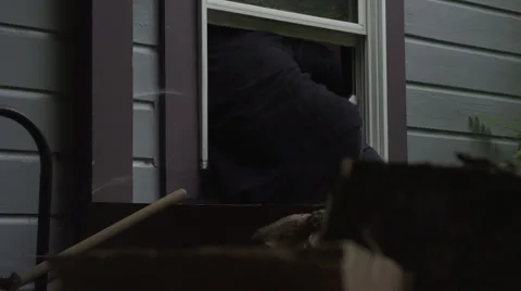 A burglar climbs through a house window Stock Footage