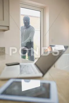 Burglar opening kitchen door and looking at laptop Stock Photos