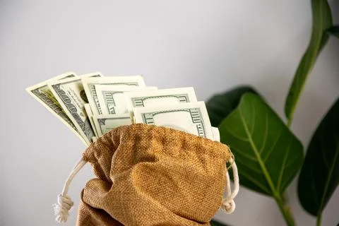 A burlap bag with a drawstring sits on a white surface, filled with US doll.. Stock Photos