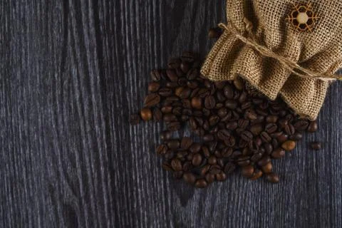 Burlap sack spilling roasted coffee beans on dark wooden surface Stock Photos
