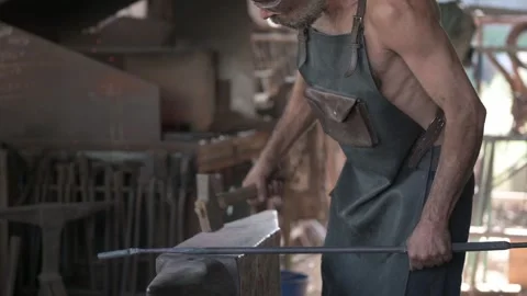 A burly blacksmith, bearded and apron-clad, expertly forging iron on his anvi Stock Footage 253201391