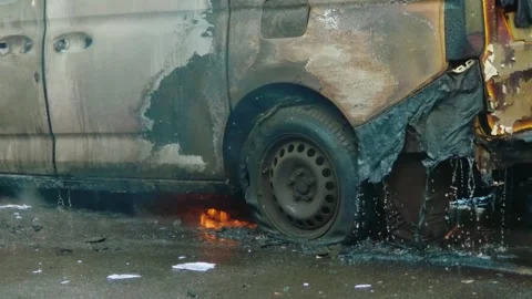 Burned car with small flames beneath damaged vehicle after severe fire. Charred Stock Footage 344104168