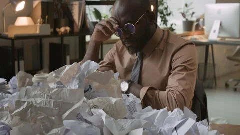 Burned Out Black Man Taking Off Glasses at Desk with Pile of Crumpled Documents Vídeo Stock 330480262
