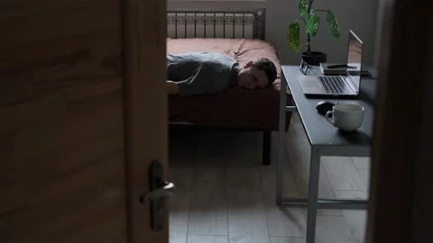Burned Out Freelancer Lying on Bed Unable to Work, Laptop and Glasses on Desk Stock Footage 310375444