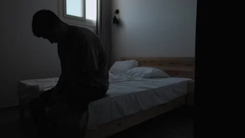 Burned out man sitting by bed with head down in emotional exhaustion Video stock 346606715