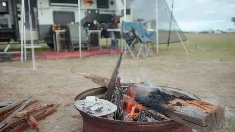 Burning camp fire scene with offroad caravan in background Stock Footage 240057486