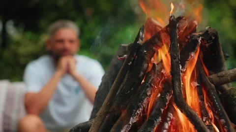 Burning Campfire with Blurred Man Sitting in Background in Forest Setting. Stock Footage 338368060