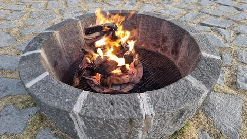 Burning campfire with bright flames inside a round outdoor stone fire pit. Stock Photos