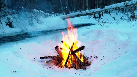 A burning campfire in winter in a snow-covered forest on the riverbank. Stock Footage 327773923