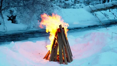 A burning campfire in winter in a snow-covered forest on the riverbank. Stock Footage 327774109