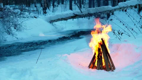 A burning campfire in winter in a snow-covered forest on the riverbank. Stock Footage 327774116