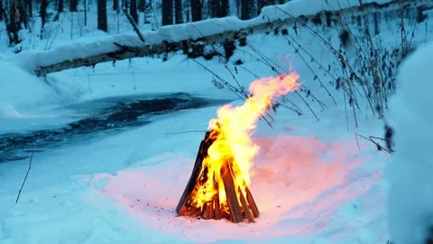 A burning campfire in winter in a snow-covered forest on the riverbank. Stock Footage 327774117