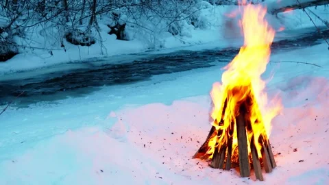 A burning campfire in winter in a snow-covered forest on the riverbank. Stock Footage 327774134