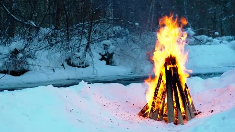 A burning campfire in winter in a snow-covered forest on the riverbank. Stock Footage 327774137