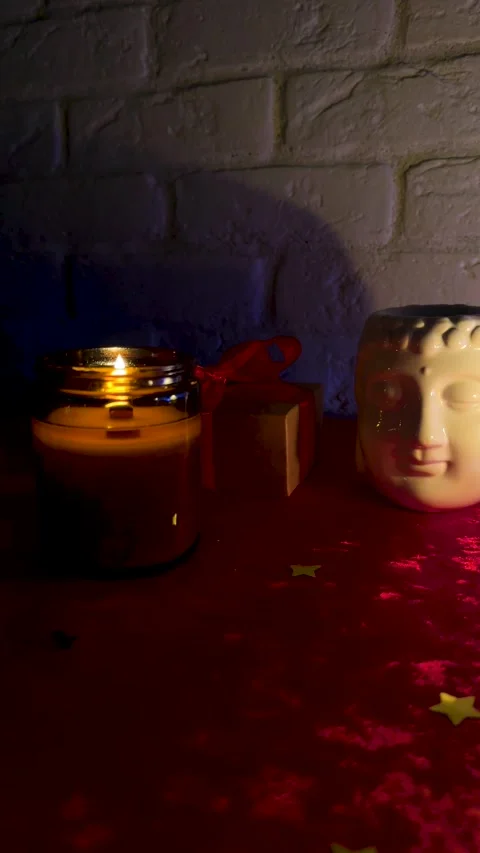 Burning candle with Buddha statue and holiday gift box with red ribbon in cozy d Stock Footage 320676903