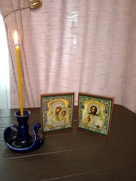 A burning candle in a candlestick and a pair of Orthodox icons depicting th.. Stock Photos