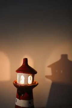 Burning candle in a candlestick in the shape of a lighthouse with a shadow, cozy Stock Photos