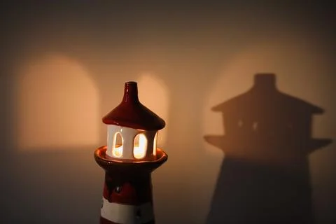 Burning candle in a candlestick in the shape of a lighthouse with a shadow, cozy Stock Photos