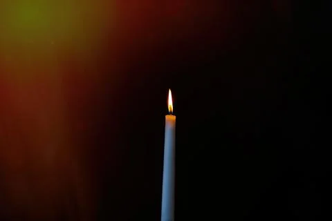 Burning candle on a dark background with light from the lights Stock Photos