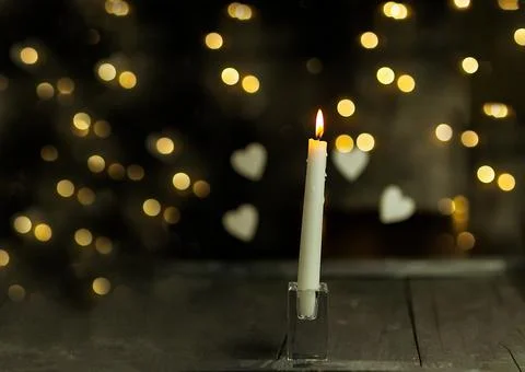 Burning candle on a dark background with light from the lights Stock Photos