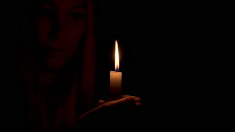 A burning candle illuminates the face of a beautiful young woman in the dark. Stock Footage 196008231