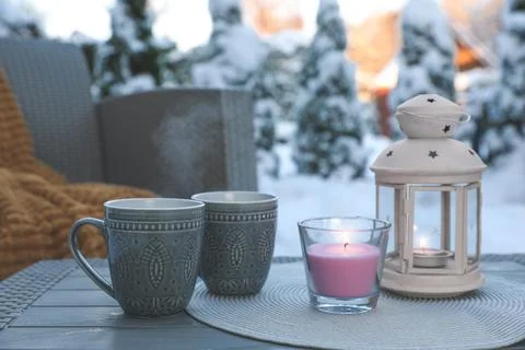 Burning candle, lantern and cups with hot drink on coffee table outdoors. C.. Stock Photos